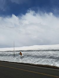 Snow covered information sign by road against cloudy sky on sunny day