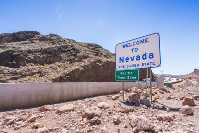 Road sign by rocks against blue sky