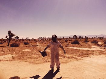 Full length of beekeeper standing in desert against sky