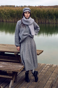 Woman stands next to the lake in a sweater and a scarf in the fall