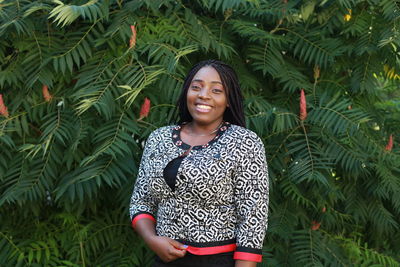 Portrait of smiling young woman standing against plants