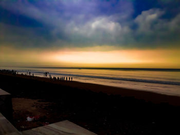 Scenic view of beach against dramatic sky during sunset