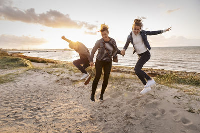 Smiling mother and children jumping at beach during weekend