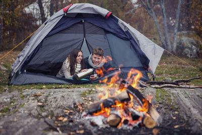 Woman pouring coffee for man while lying in tent at forest