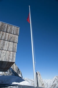 Low angle view of flag on snowcapped mountains against clear blue sky