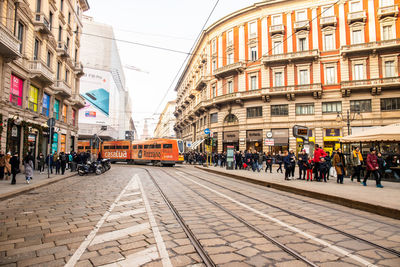 People walking on railroad tracks amidst buildings in city