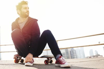 Full length of young man sitting on railing against sky