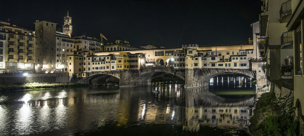 Arch bridge over river amidst buildings in city at night