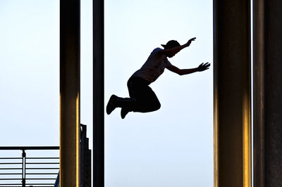 Low angle view of silhouette man jumping against clear sky