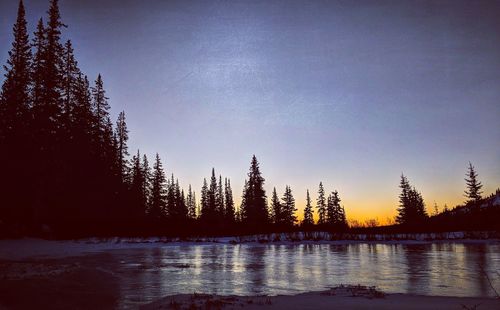 Silhouette trees by lake against sky at sunset