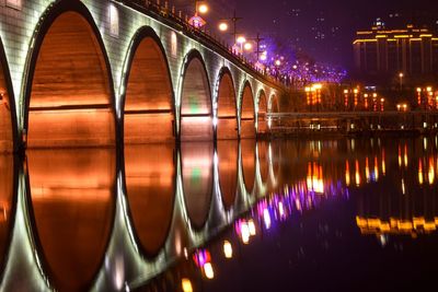 Illuminated bridge over river in city at night
