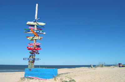 Information sign at beach against clear blue sky