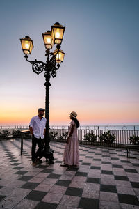 People standing on street against sky at sunset