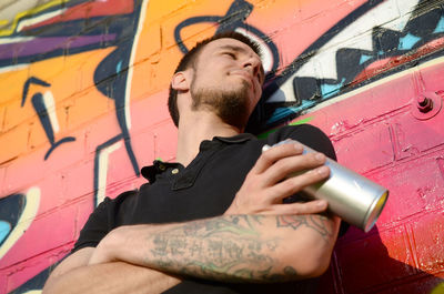 Young man looking away while standing against graffiti wall