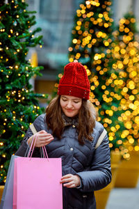 Woman wearing hat standing against illuminated christmas tree during winter