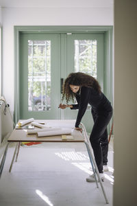 Side view of female design professional doing multi-tasking while working at under construction apartment