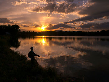 Silhouette man standing by lake against sky during sunset