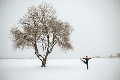 Remote view of flexible female practicing yoga in utthita hasta padangushthasana while standing on snowy field in winter