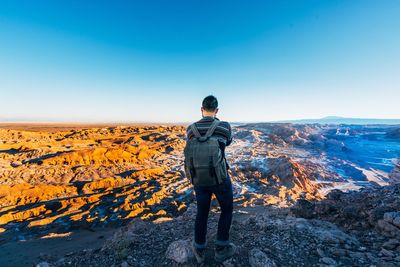 Rear view of man standing on mountain against clear sky