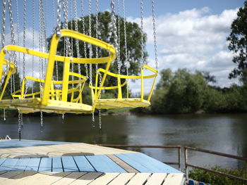 Empty swings by lake against sky