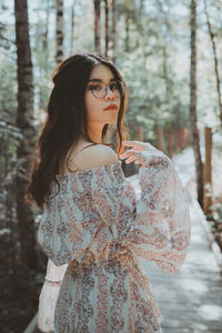 Beautiful young woman standing by tree in forest