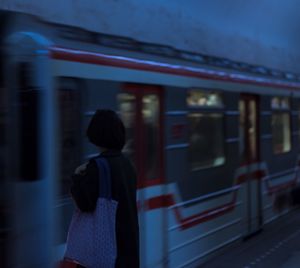 Rear view of woman standing in front of train at railroad station