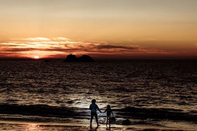 People on beach against sky during sunset