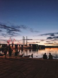 People by sea against sky during sunset