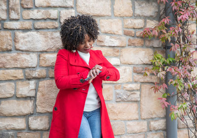 Serious african american woman looks impatiently at her wrist watch near house