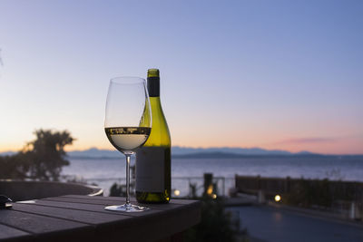 Close-up of wineglass with bottle on table against sky