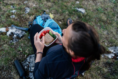 Rear view of man holding food while sitting on land