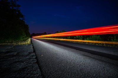 Light trails on road against clear sky at night