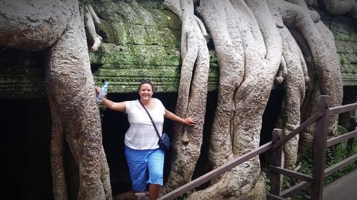 Portrait of young woman standing on tree trunk