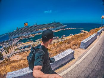 Rear view of man sitting by sea against blue sky