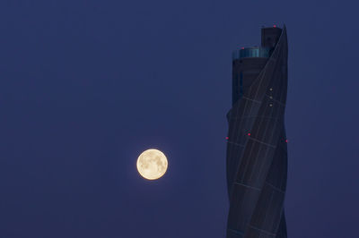 Low angle view of moon and buildings against sky at night