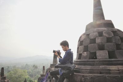 Man using camera while standing on temple against sky