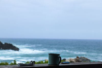 Cup on railing with sea in background against sky