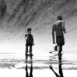 Rear view of men standing on puddle at beach