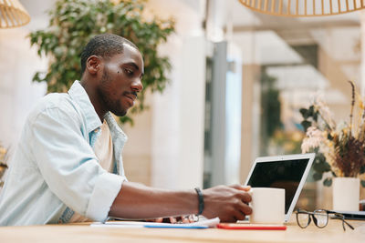 Side view of young man using laptop at table