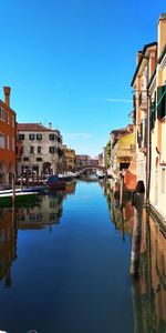 Canal amidst buildings against blue sky