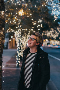 Young man wearing sunglasses against illuminated tree at night