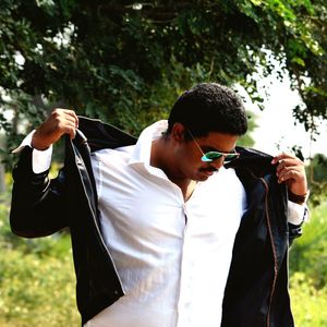 Young man wearing jacket while standing against trees