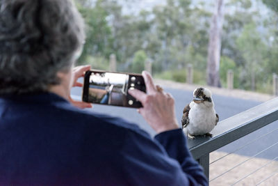 Rear view of woman photographing bird through mobile phone