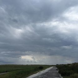 Road passing through field against cloudy sky