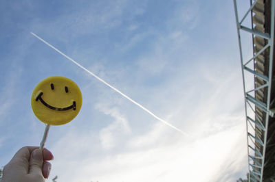 Low angle view of hand holding candy against vapor trail in sky