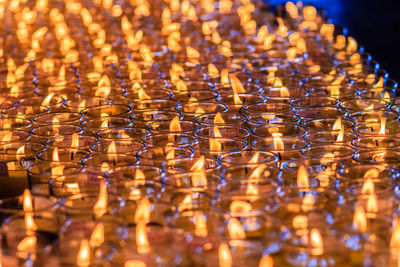 Full frame shot of illuminated candles in glasses at church