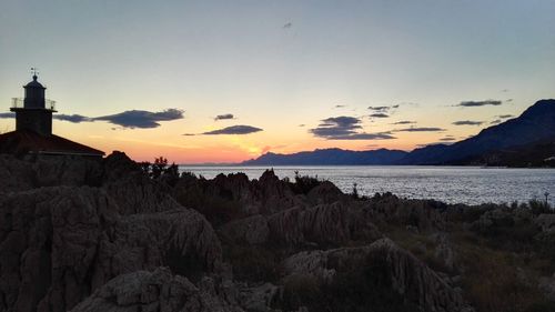 Lighthouse and rocks by adriatic sea against sky at dusk