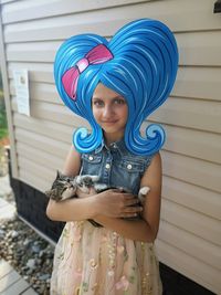 A girl with blue hair holds a kitten in her hands