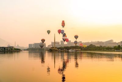 Hot air balloon flying over lake against sky during sunset