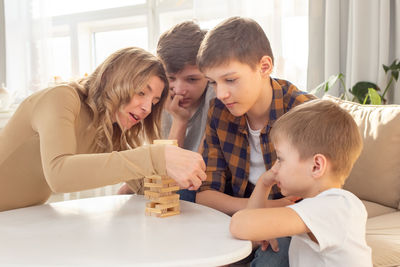 A  woman and three sons are enthusiastically playing a board game made of wooden rectangular blocks